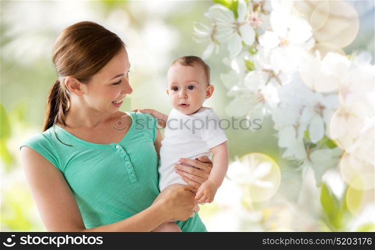 family, child and parenthood concept - happy smiling young mother with little baby over natural cherry blossoms background. happy young mother with baby over cherry blossoms