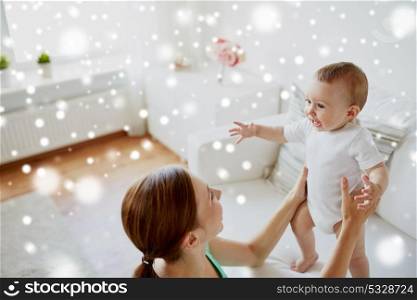 family, child and parenthood concept - happy smiling young mother with little baby at home over snow. happy young mother with little baby at home