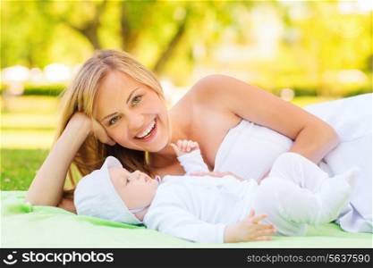 family, child and parenthood concept - laughing mother lying with little baby on blanket in park