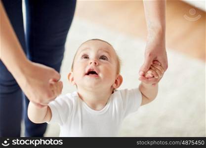family, child, childhood and parenthood concept - close up of happy little baby learning to walk with mother help at home