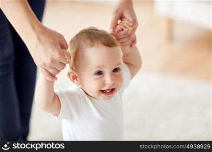 family, child, childhood and parenthood concept - close up of happy little baby learning to walk with mother help at home. happy baby learning to walk with mother help