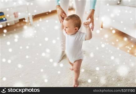 family, child, childhood and parenthood concept - happy little baby learning to walk with mother help at home over snow. happy baby learning to walk with mother help