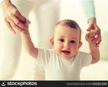family, child, childhood and parenthood concept - happy little baby learning to walk with mother help at home. happy baby learning to walk with mother help