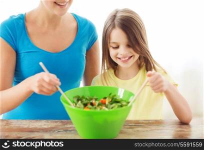 family, child, cooking and home concept - smiling little girl with mother mixing salad in the kitchen