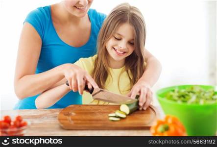 family, child, cooking and home concept - smiling little girl with mother chopping cucumber in the kitchen