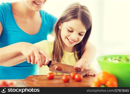 family, child, cooking and home concept - smiling little girl with mother chopping tomatoes in the kitchen