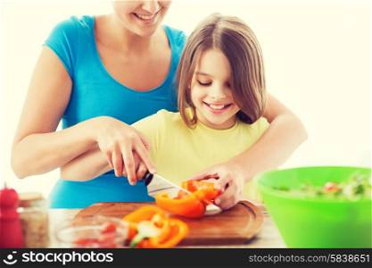 family, child, cooking and home concept - smiling little girl with mother chopping pepper in the kitchen