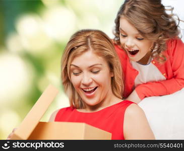 family, child, holiday and party concept - smiling mother and daughter opening gift box