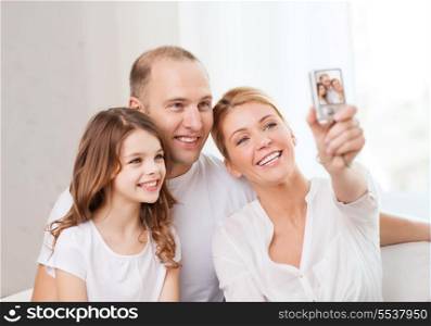 family, child, photography and home concept - happy family with little girl making self portrait with digital camera