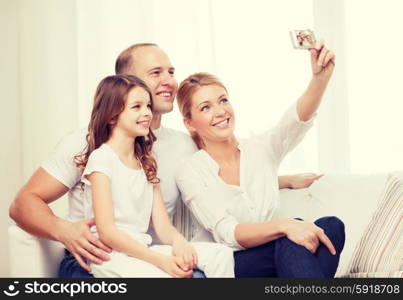 family, child, photography and home concept - happy family with little girl making self portrait with digital camera