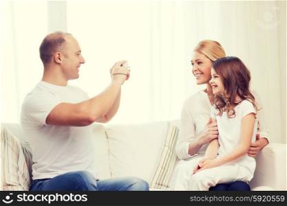 family, child, photography and home concept - smiling happy father taking picture of mother and daughter