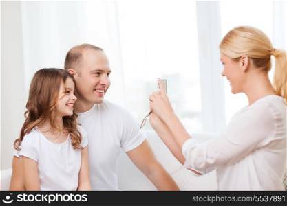 family, child, photography and home concept - smiling happy mother taking picture of father and daughter