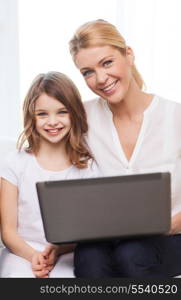 family, child, technology and home concept - smiling mother and little girl with laptop at home
