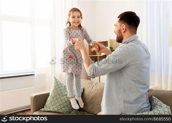 family, childhood and fatherhood concept - happy father and little daughter jumping on sofa and having fun at home. father and daughter jumping and having fun at home