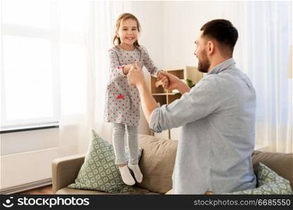 family, childhood and fatherhood concept - happy father and little daughter jumping on sofa and having fun at home. father and daughter jumping and having fun at home