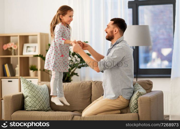 family, childhood and fatherhood concept - happy father and little daughter jumping on sofa and having fun at home. father and daughter jumping and having fun at home