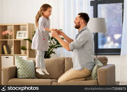 family, childhood and fatherhood concept - happy father and little daughter jumping on sofa and having fun at home. father and daughter jumping and having fun at home