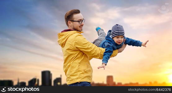 family, childhood and fatherhood concept - happy father and little son playing and having fun outdoors over evening tallinn city background. father with son playing and having fun outdoors