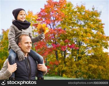 family, childhood and fatherhood concept - happy father carrying son with maple leaves over autumn park background. happy father carrying son with autumn maple leaves