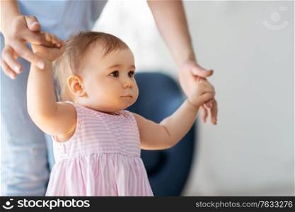family, childhood and motherhood concept - little baby girl learning to walk with mother&rsquo;s help at home. baby girl learning to walk with mother&rsquo;s help