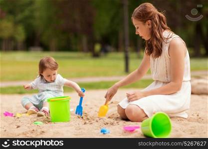family, childhood and parenthood concept - happy mother and little baby girl with sand toys playing in sandbox at summer playground. happy mother and baby girl playing in sandbox