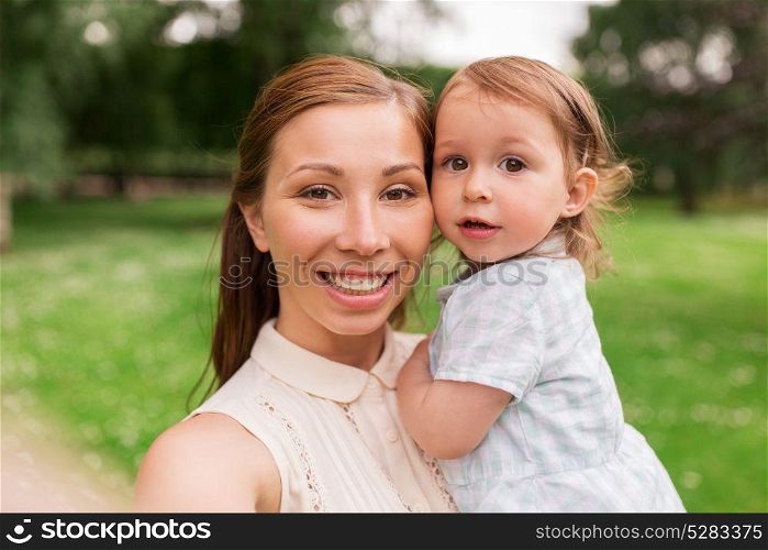 family, childhood and parenthood concept - happy mother holding little baby girl and taking selfie at summer park. mother with baby girl taking selfie at summer park