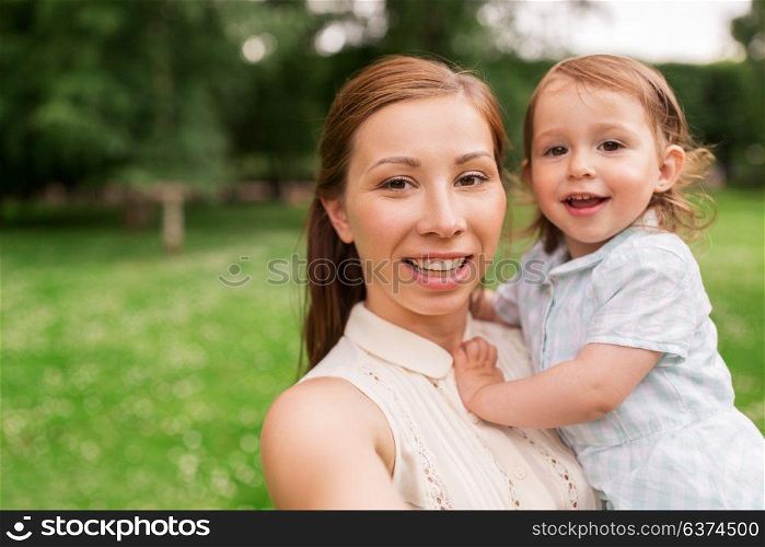family, childhood and parenthood concept - happy mother holding little baby girl and taking selfie at summer park. mother with baby girl taking selfie at summer park