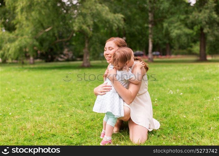 family, childhood and parenthood concept - happy mother hugging little baby girl at summer park. happy mother hugging baby girl at summer park