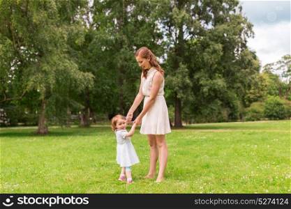 family, childhood and parenthood concept - happy mother with little baby girl playing and having fun at summer park. happy mother playing with baby girl at summer park