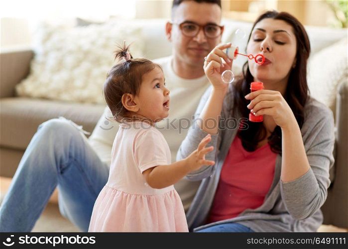 family, childhood and people concept - happy mother blowing soap bubbles and playing with little daughter at home. family with soap bubbles playing at home. family with soap bubbles playing at home