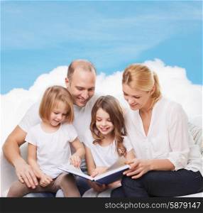 family, childhood, dream and people - smiling mother, father and little girls reading book over blue sky and cloud background
