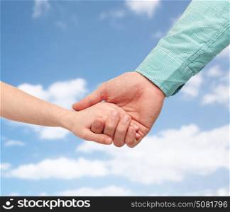 family, childhood, fatherhood and people concept - father and child holding hands over blue sky and clouds background. father and child holding hands over blue sky
