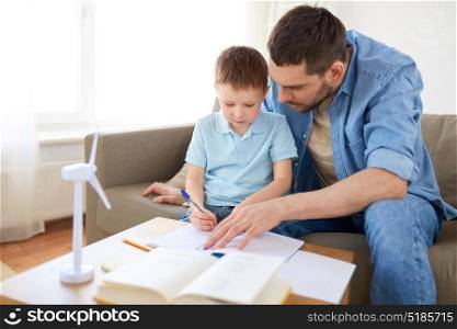 family, childhood, fatherhood and people concept - father and little with toy wind turbine drawing to notebook at home. father and son with toy wind turbine at home