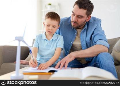 family, childhood, fatherhood and people concept - father and little with toy wind turbine drawing to notebook at home. father and son with toy wind turbine at home