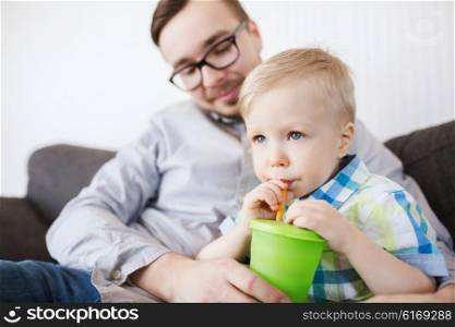 family, childhood, fatherhood, care and people concept - father helping little son with drinking from cup at home