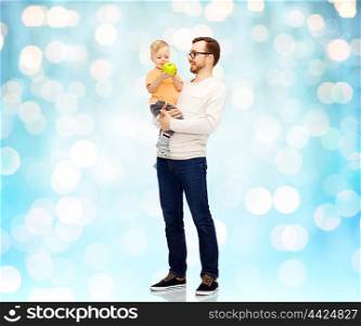 family, childhood, fatherhood, healthy eating and people concept - happy father and and little son with green apple over blue holidays lights background