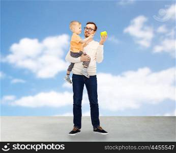 family, childhood, fatherhood, healthy eating and people concept - happy father and and little son with green apple over blue sky and clouds background