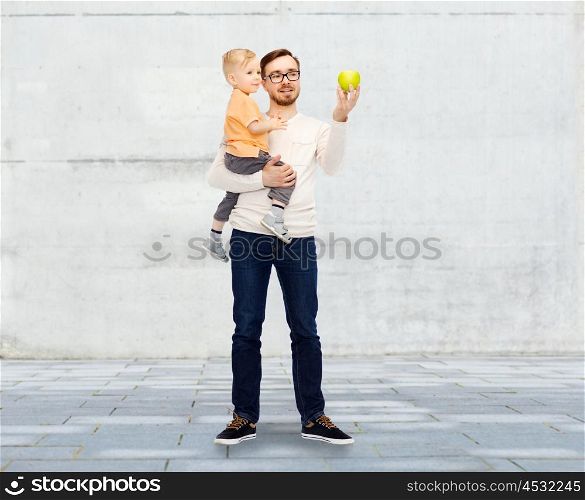 family, childhood, fatherhood, healthy eating and people concept - happy father and and little son with green apple over urban street background