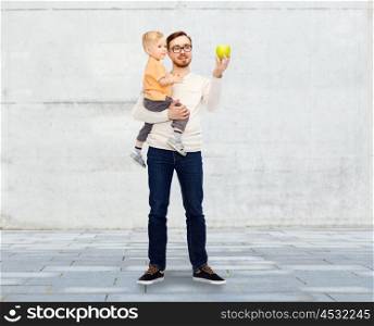 family, childhood, fatherhood, healthy eating and people concept - happy father and and little son with green apple over urban street background