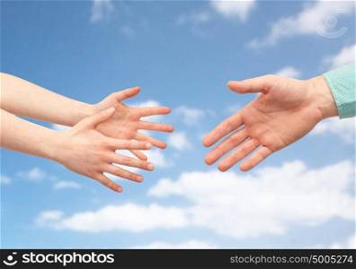 family, childhood, fatherhood, help and people concept - father and child hands over blue sky and clouds background. father and child hands over blue sky