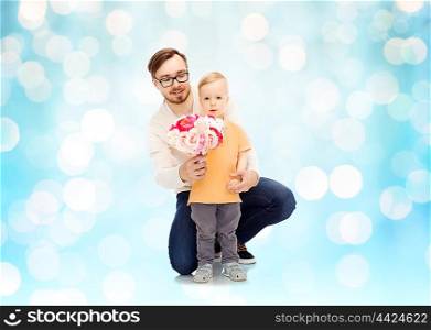 family, childhood, fatherhood, holidays and people concept - happy father and and little son with bunch of flowers over blue holidays lights background