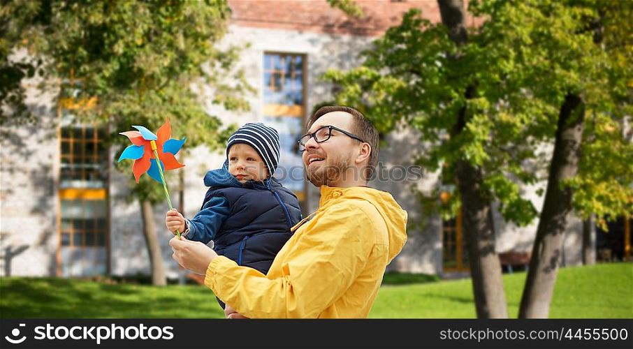 family, childhood, fatherhood, leisure and people concept - happy father and little son with pinwheel toy outdoors over summer city yard background