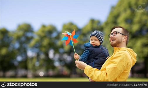 family, childhood, fatherhood, leisure and people concept - happy father and little son with pinwheel toy outdoors over summer park background
