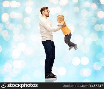 family, childhood, fatherhood, leisure and people concept - happy father and little son playing and having fun over blue holidays lights background