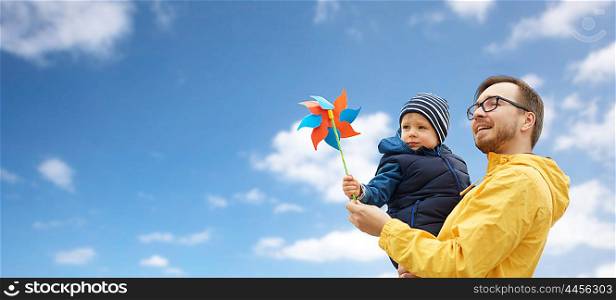 family, childhood, fatherhood, leisure and people concept - happy father and little son with pinwheel toy over blue sky and clouds background