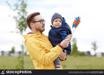 family, childhood, fatherhood, leisure and people concept - happy father and little son with pinwheel toy outdoors