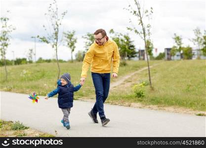family, childhood, fatherhood, leisure and people concept - happy father and little son with pinwheel toy walking outdoors