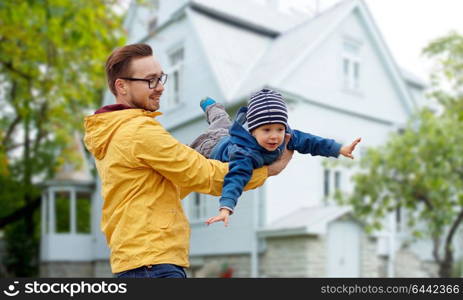 family, childhood, fatherhood, leisure and people concept - happy father and little son playing and having fun outdoors over house background. father with son playing and having fun outdoors