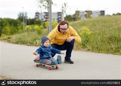family, childhood, fatherhood, leisure and people concept - happy father and little son riding on skateboard