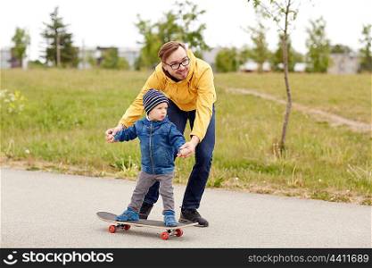 family, childhood, fatherhood, leisure and people concept - happy father teaching little son to ride on skateboard